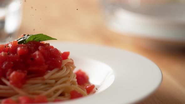 Camera follows grinding pepper over fresh tomato sauce spaghetti in plate. Slow Motion.