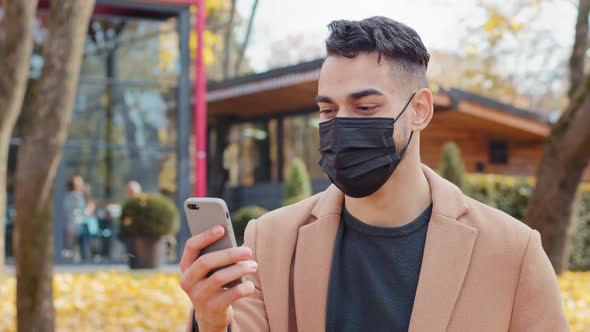 Spanish Young Man in Medical Mask Talking on Video Call Using Smartphone Standing in Park Hispanic