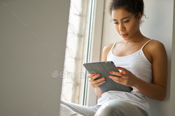 Focused young mixed race woman reading a book using tablet pc / Photodune, Misc
