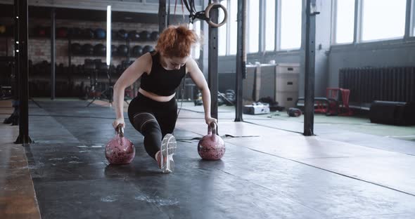 Young Professional Athletic Red Haired Coach Woman Doing Split Stretch Exercise on Kettlebells in