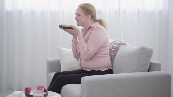 Side View Wide Shot of Redhead Adult Woman Smelling and Biting Delicious Bun. Fat Caucasian Senior