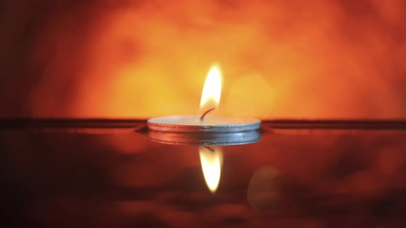 A small candle floating in the wavy water in the darkness