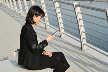 ng fashionable elegant clothes sitting outdoors checking her workflow plan on smartphone, copy space