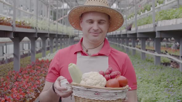 Smiling Man with Vegetable Basket Stretching Bottle with Pesticides To Camera. Portrait of Confident