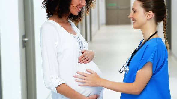 Doctor touching pregnant womans belly in corridor