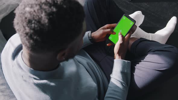 High Angle View of a Man Sitting Crosslegged on a Couch Using His Cell Phone