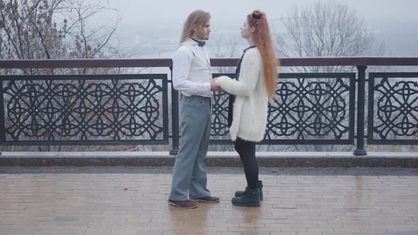 Side View of Young Caucasian Man Taking His Girlfriend's Hands and Talking