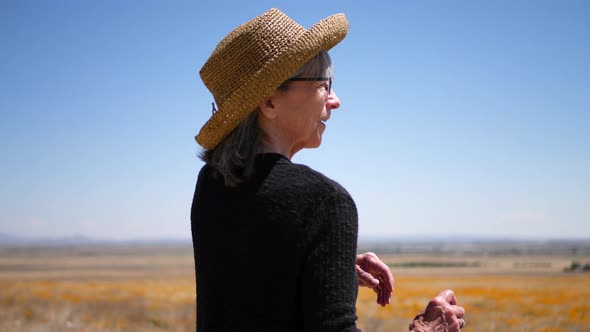 A smiling old woman with gray hair laughing in a summer field of orange flowers under blue sky SLOW