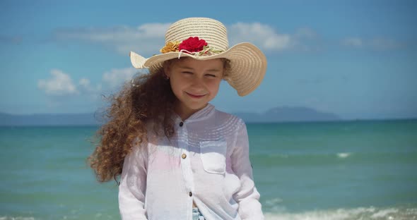 Portrait of a Funny Little Girl in a Hat a Smiling Child Looking at the Camera Stands on the Beach