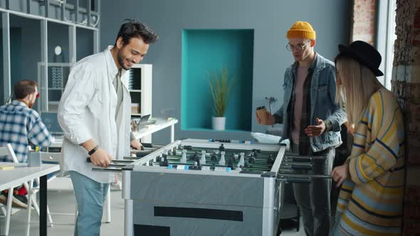 Joyful Colleagues Playing Table Soccer Then Laughing and Doing Highfive Indoors in Office