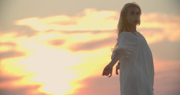 Colorful Sunset Sky in the Background of a Woman in White Dress Dancing