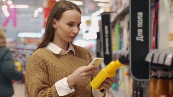 Woman Scans the Barcode on a Bottle of Detergent with Her Smartphone While Shopping at the