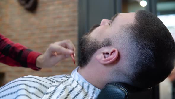 The Client is Sitting in a Hairdresser's Chair While Cutting His Beard