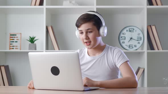 Smiling Boy in Headphones Chatting Online By Video Call with Laptop Computer at Home While Sitting