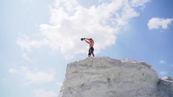 Strong man lifting kettlebell on the mountain in summer.