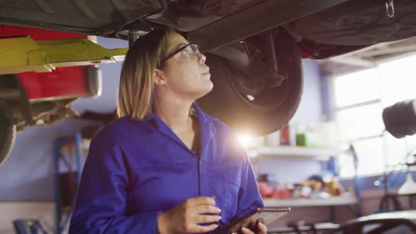 Female mechanic using digital tablet standing under a car at a car service station