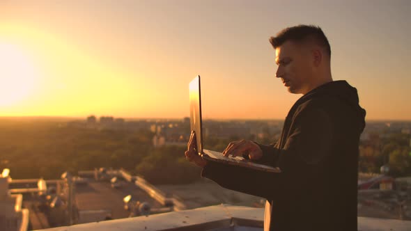 Hacker Using Laptop on Rooftop with City View and Forex Chart. Hacking and Stats Concept