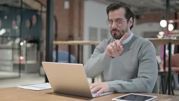 Young Man Shaking Head As No Sign While Using Laptop in Office