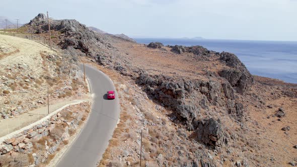 Drone shot of car driving along the narrow coastal road above rocky shore towards volcanic mountains