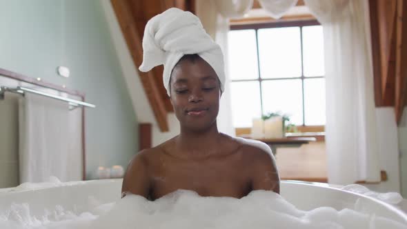 Happy african american attractive woman relaxing in foam bath in bathroom