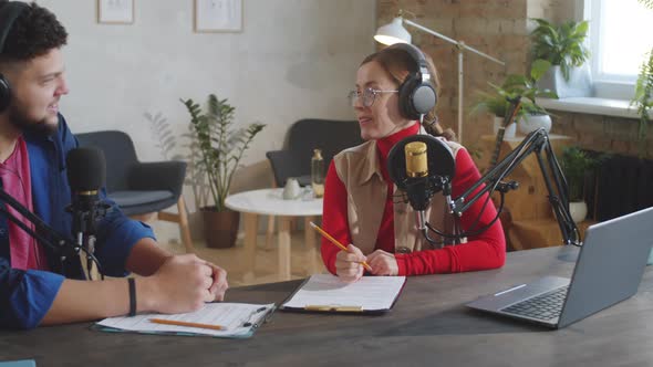 Two Podcast Presenters Speaking into Mics in Recording Studio