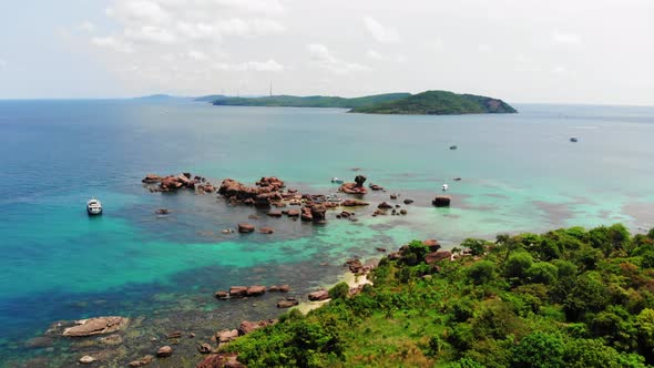 Boat Anchored in Clear Turquoise Sea Waters next to Rocks and Rocky Coast of Gam Ghi island in Vietn