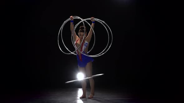 Gymnast Twists a Lot of Hoops and One Hoop on Her Legs. Black Background