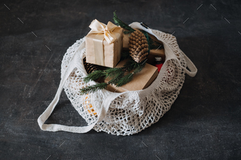 tmas. Eco friendly mesh net shopping bag with craft gift boxes and green fir tree branch. Mesh Reusable Cotton Grocery Bag with Christmas gifts.