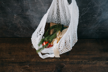 tmas. Eco friendly mesh net shopping bag with craft gift boxes and green fir tree branch. Mesh Reusable Cotton Grocery Bag with Christmas gifts.
