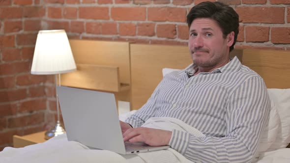 Middle Aged Man with Laptop Saying No by Head Shake in Bed