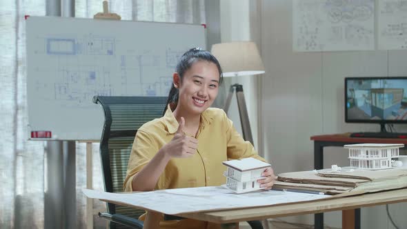 Asian Woman Engineer Holding Paper Model Of House Warmly Smiling And Showing Thumb Up To Camera