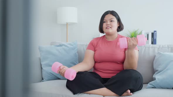 Asian young plus size girl exercise to lose weight by use dumbbell workout in living room at home.