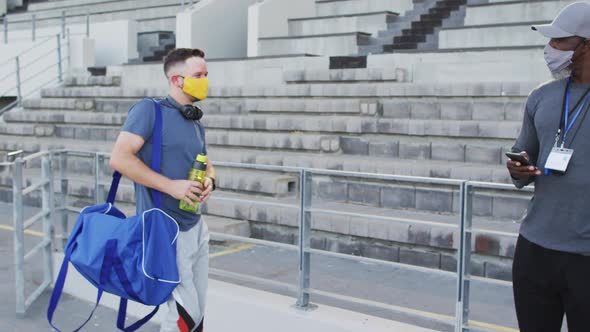 Diverse male coach and disabled athlete wearing face mask touching elbows before training session