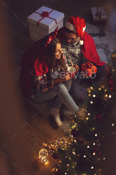 a nicely decorated Christmas tree, covered with soft red blanket, hugging, drinking hot tea and exchanging presents