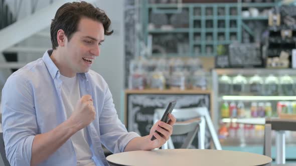 Creative Man Celebrating on Smartphone in Cafe