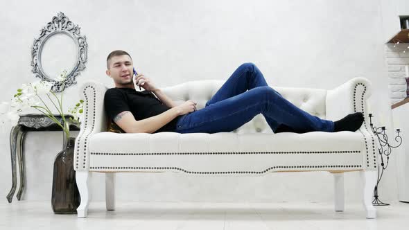 Young Man Relaxing on Couch and Speaks By Mobile Phone in Modern Luxury House