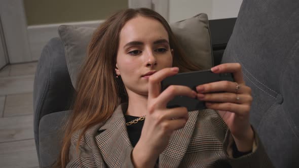 Relaxed Girl Holding Smartphone Using Mobile Apps Play Games Watching Video Lying on Couch at Home