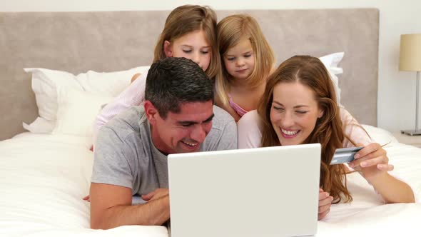 Parents and Daughters Lying on Bed Shopping Online with Laptop