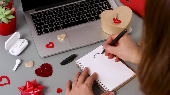 Young woman drawing a heart in a notebook while wrapping valentine's day gift