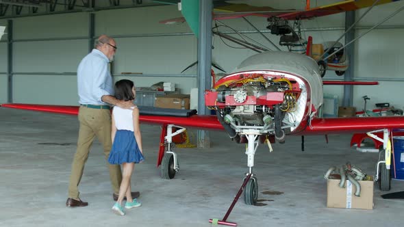 Grandfather showing his granddaughter sports plane in hangar