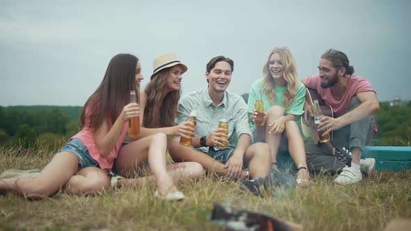 Happy Friends Drinking Beer, Having Fun And Sitting Near Bonfire