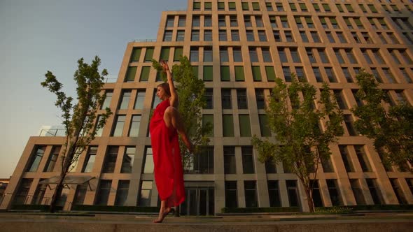 Beautiful Young Girl Dancing on the Street of a Modern Building of a Business Center in the Sunset