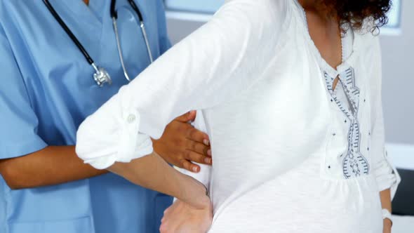 Doctor examining pregnant womans back in ward