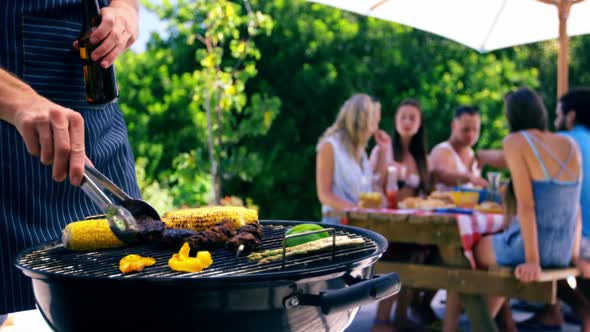 Mid section of man grilling corn, meat and vegetable on barbecue