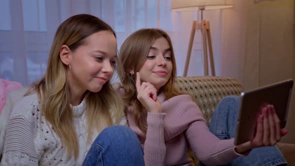 Pretty Young Caucasian Women Sitting on Couch in Living Room and Talking Via Webcam on Tablet Device