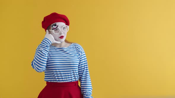 Actress mime talks to her hand as if on phone and shows OK gesture to the camera, on an orange backg