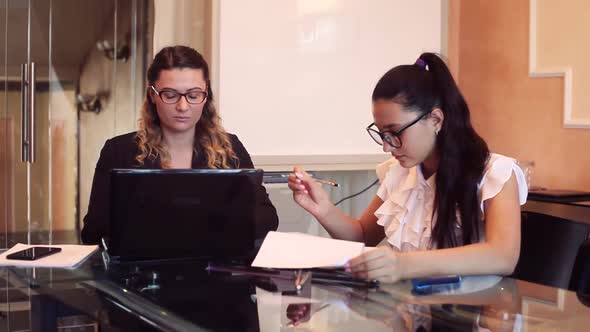 Two Business Women Wearing Glasses in Business Clothes Working on a Business Project in an Office