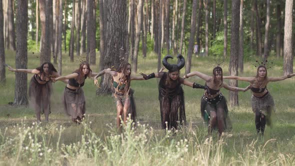 Young Women in Theatrical Costumes of Forest Dwellers or Devils Dancing in Forest Showing Perfomance