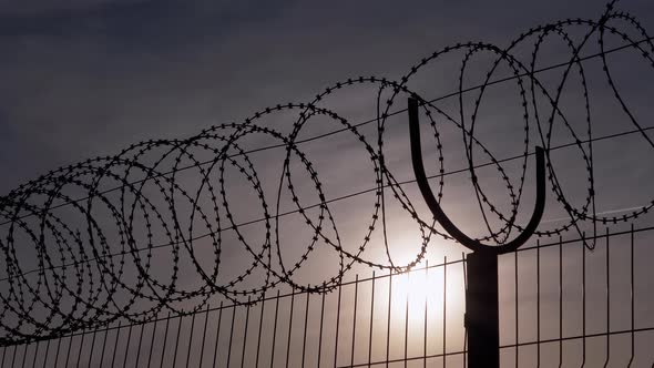 Barbed Wire Hangs on Border of a Iron Fence Against the Backdrop of Sunset