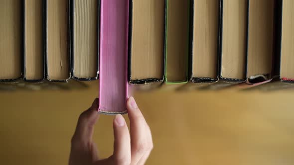 A girl takes a book with pink pages from a shelf and puts it back in a row